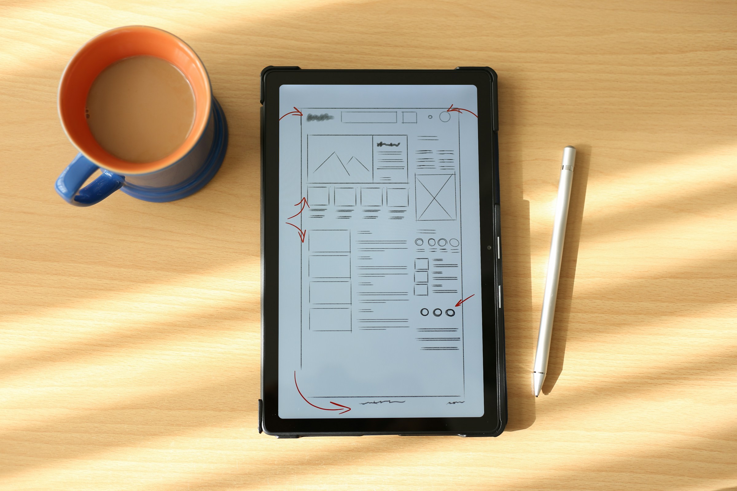 An image of wireframes on an ipad next to a cup of coffee.