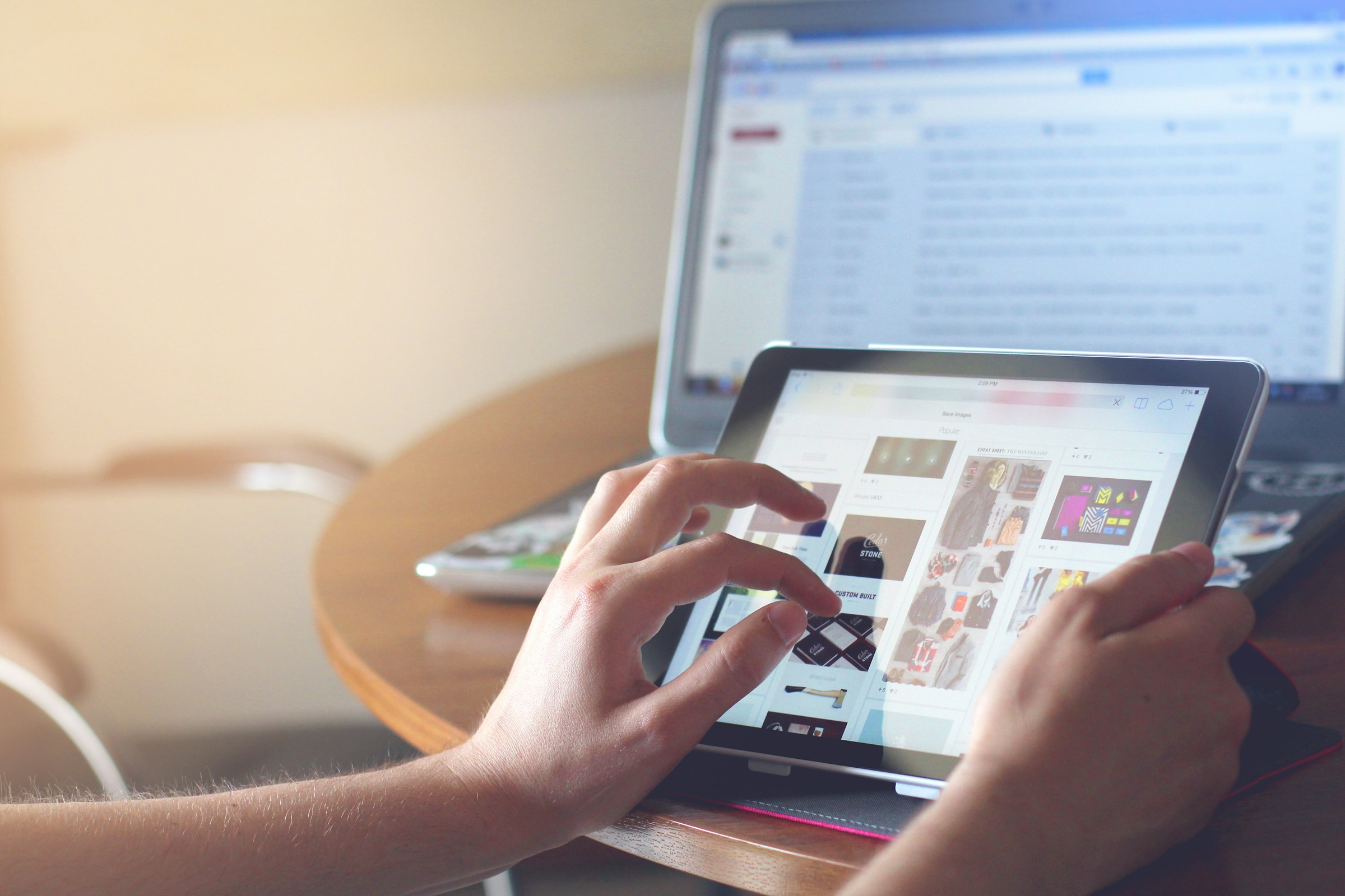 A pair of hands using their tablet and laptop to navigate a website 
